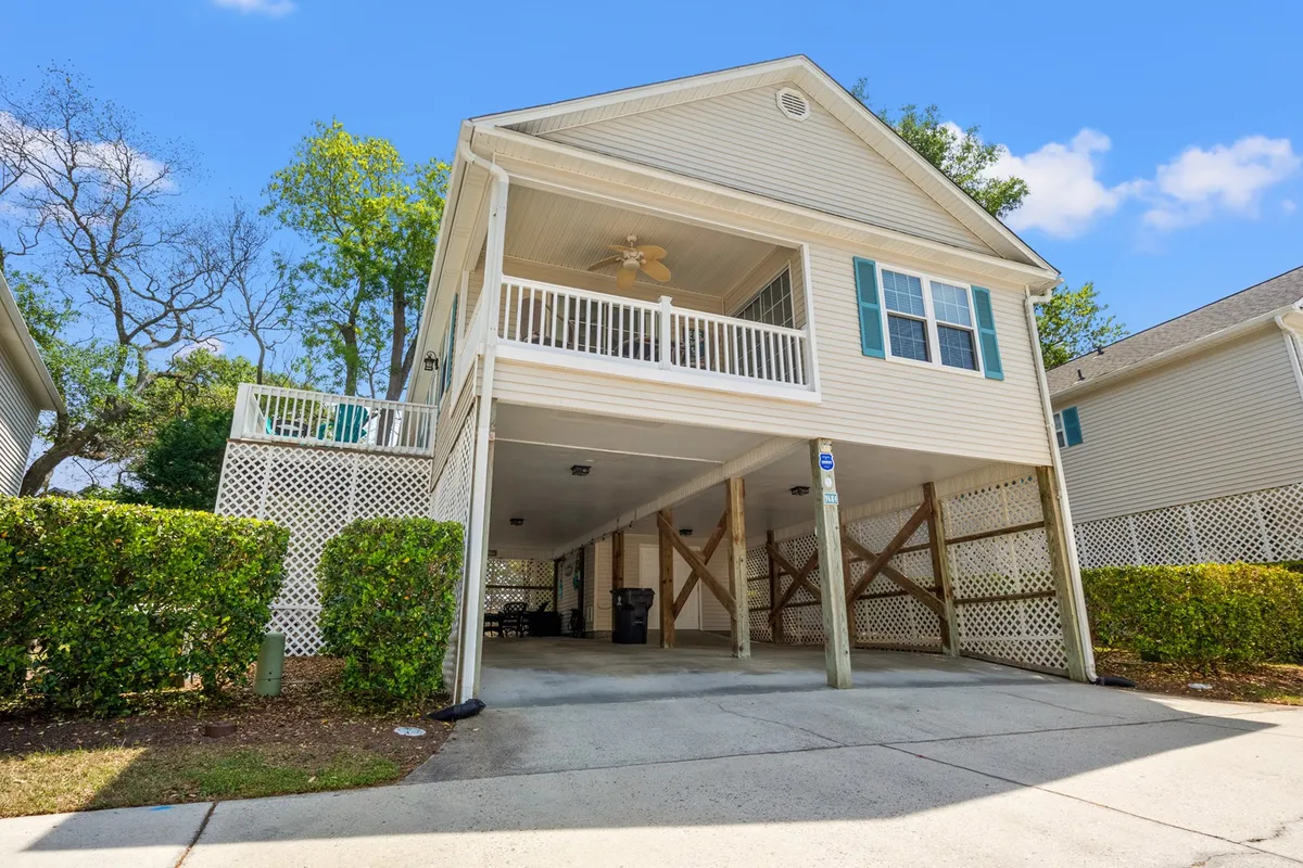 A charming exterior shot of a private cottage with an elevated porch, green shutters, and lush surrounding greenery. The scene exudes a welcoming and peaceful neighborhood ambiance, ideal for quiet mornings or relaxing after a day out.
