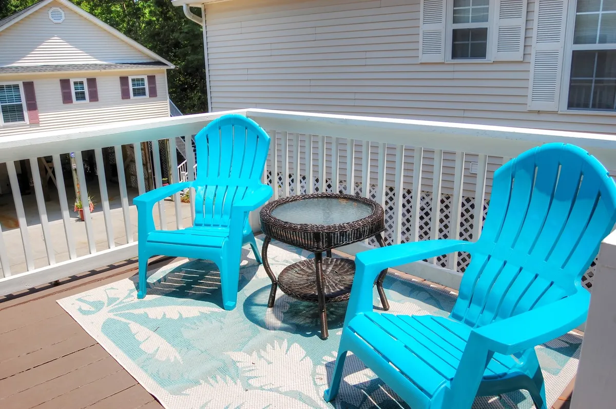 An exterior patio scene featuring turquoise chairs and a glass table set atop a decorative rug. The setup is inviting for both sunrise coffee moments and evening stargazing, surrounded by outdoor views that encourage relaxation and social connection.