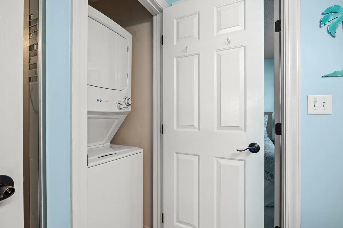 This image shows a stacked washer and dryer tucked neatly into a nook with white doors and a light blue wall. The setup is clean, inviting, and suggests the convenience of in-unit laundry.