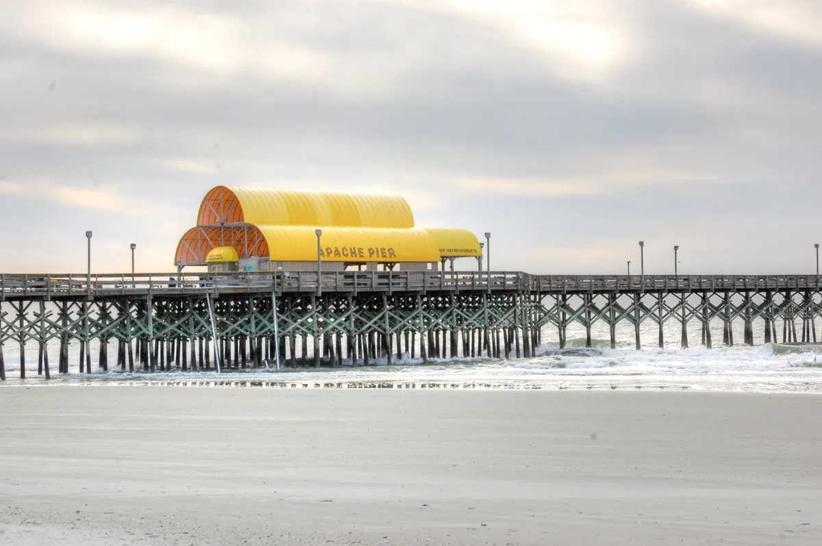 A scenic exterior view of the Apache Pier with its distinctive yellow roof stretching over water and waves, ideal for fishing, walking, or people-watching. The pier is a local landmark encouraging exploration and a sense of community beyond the cottages themselves.