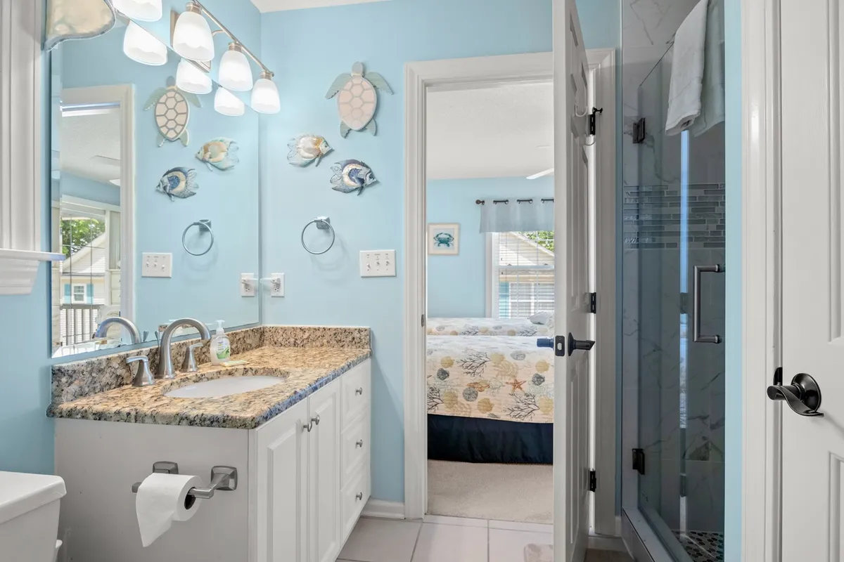 A well-appointed bathroom with a granite countertop, stylish light fixtures, decorative fish and turtle wall art, and an open shower area. The overall environment is cheerful and functional, suited to shared morning routines or unwinding after a day outdoors.