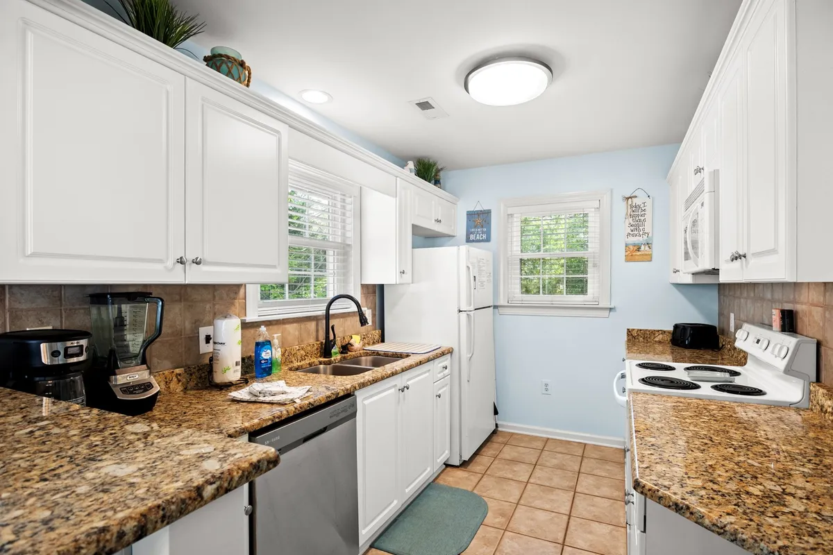 A cozy kitchen scene showing granite countertops, a kitchen sink, white cabinetry, and appliances. The setting exudes warmth and functionality, ideal for family gatherings or everyday meal prep.