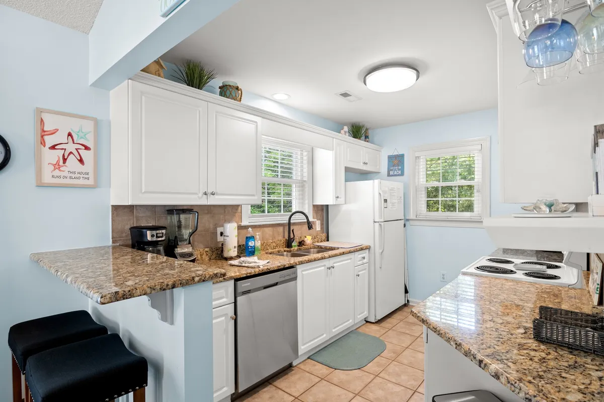 This image features a bright kitchen with granite countertops, white cabinetry, various kitchen appliances, and a window that lets in natural light. The layout suggests ample counter space and a welcoming environment for both meal prep and gatherings.