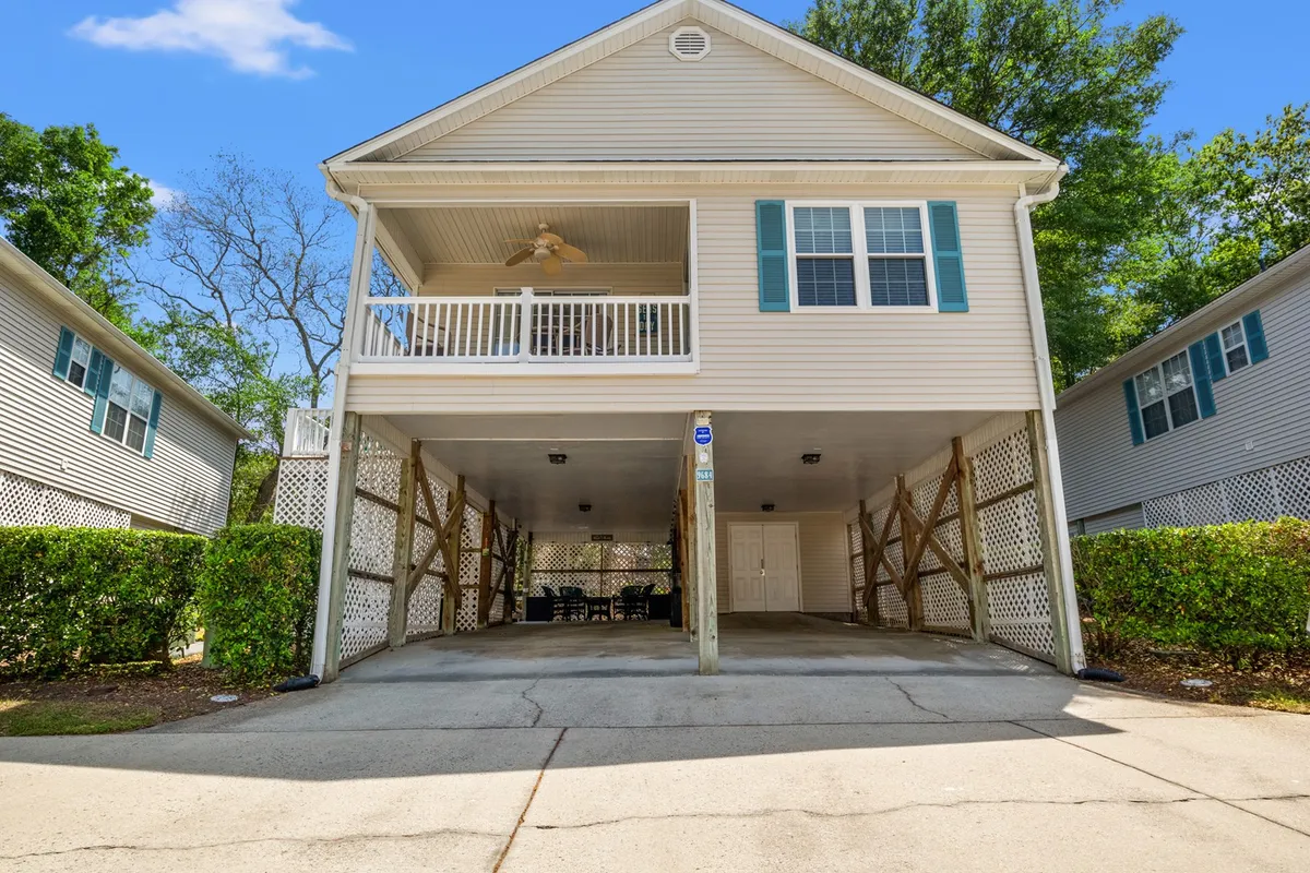 This exterior image captures the front porch and under-house carport of a cottage, with landscaped hedges adding a welcoming touch. The carport clearly shows available covered parking, and the porch hints at the relaxed, resort-style atmosphere the section describes.