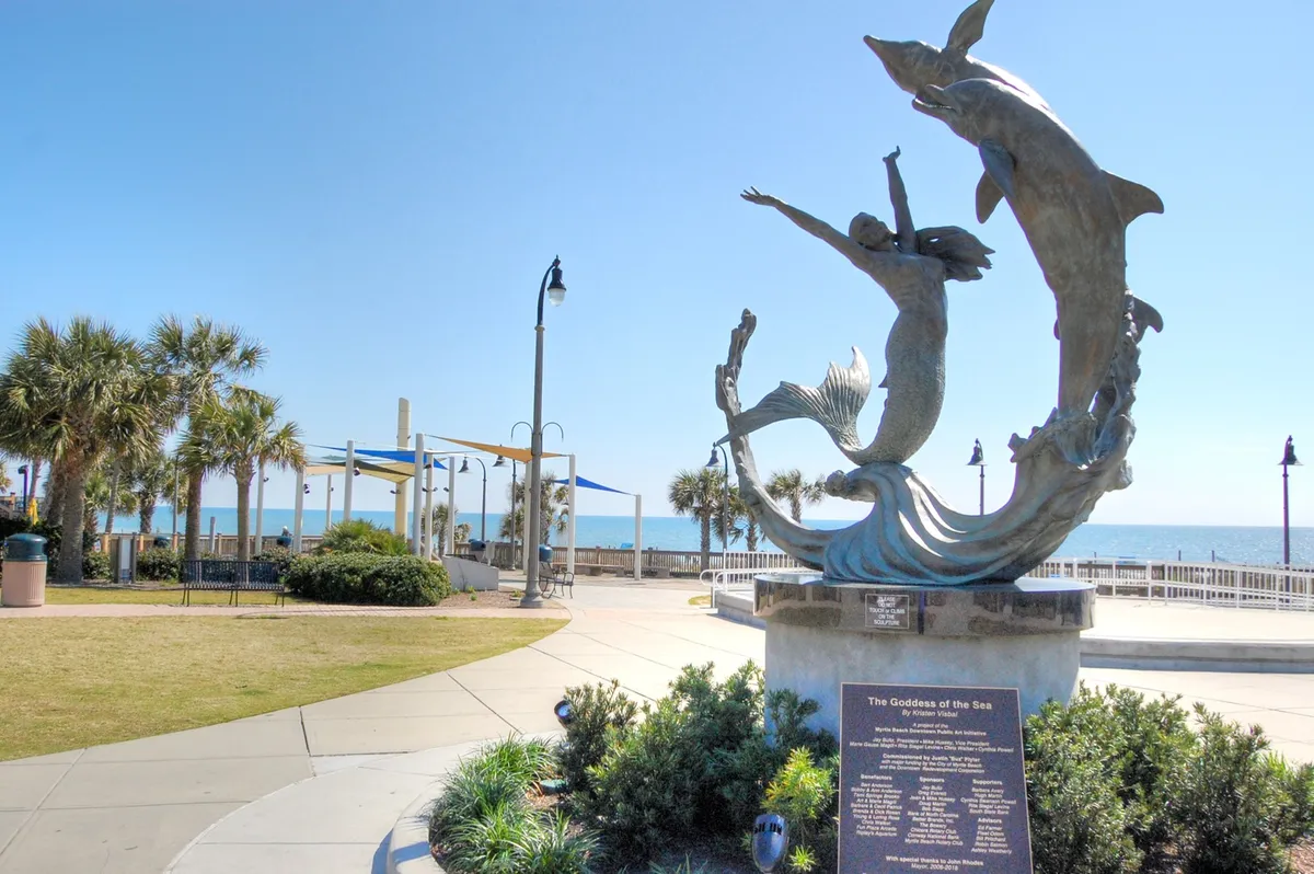 An exterior perspective showcasing a sculpture of the Goddess of the Sea surrounded by dolphins, palm trees, and a wide ocean view. The promenade setting encourages outdoor exploration, socializing, and participation in local events and festivals.
